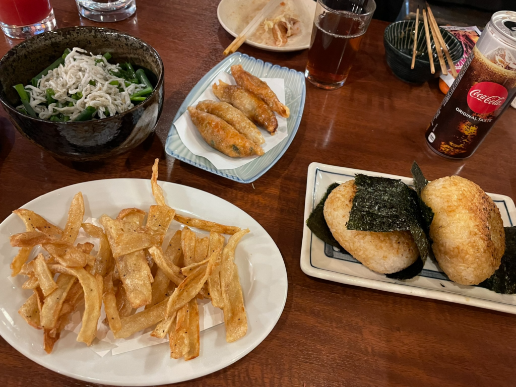 きも善のテーブルに並ぶ、焼きおにぎり、フライド大和芋など様々な居酒屋料理とコカ・コーラの缶。