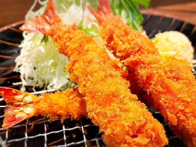 タルタルソースが添えられた、黄金色に揚げられた大きなエビフライのイラスト。