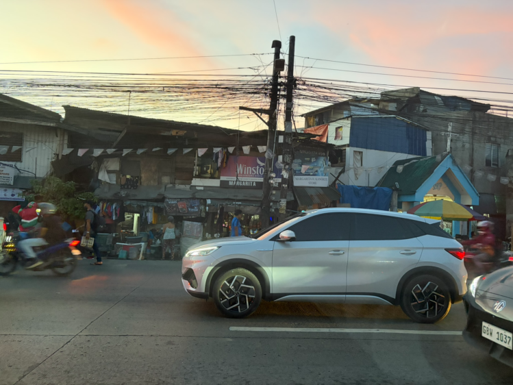 夕暮れ時のフィリピンの街並みと、道路に停車しているシルバーの車の様子。