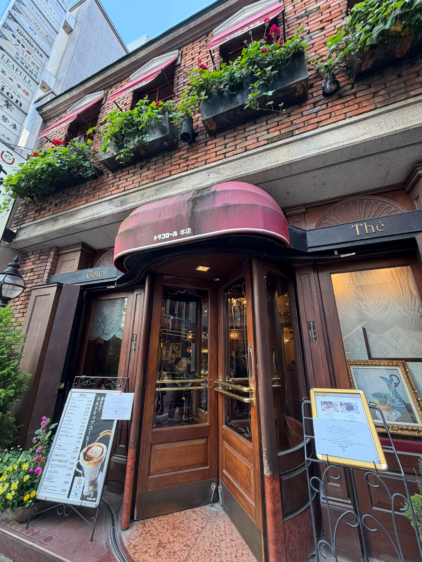 銀座トリコロール本店の外観。赤いオーニング、花の咲いたプランター、木製の回転扉、メニュー看板が見える。