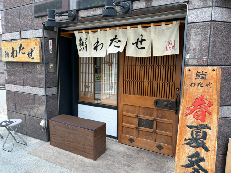 横浜・関内にある「鮨わたせ」の店舗外観。石壁に白い暖簾と木製の看板が設置された趣のある入り口。
