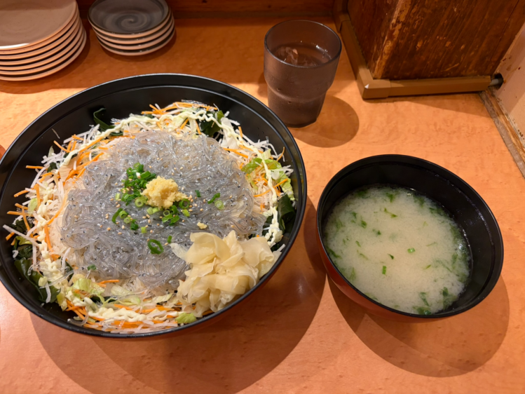 木目のテーブルの上に並んだ、ボリューム満点の生シラス丼、アオサの入ったお味噌汁、お水のグラス。