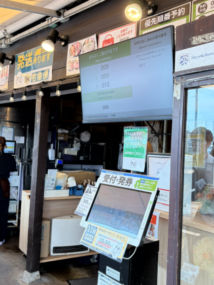 店頭に設置されたEPARKの受付・発券機と、その上に設置された「まもなくご案内予定です」と現在の待ち組数を表示する案内モニター。