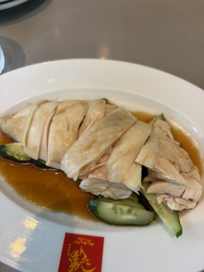 白いお皿にきれいにスライスして盛り付けられた、タレがかかったスチームチキン(海南鶏飯のチキン)のアップ。