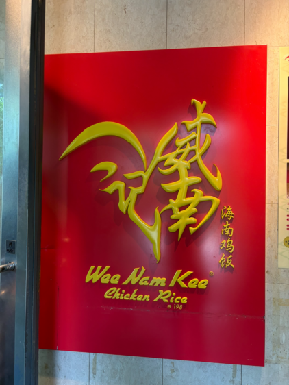 「Wee Nam Kee Chicken Rice」と中国語で書かれた、赤地に黄色の立体的で特徴的なロゴ看板。
