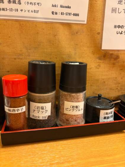 黒いトレーに載った4種類の調味料ボトル。左から一味唐辛子、（岩塩）ナマック、（岩塩）ピンクソルト、そして（海水塩）粟国の塩。それぞれの日本語ラベルがはっきりと読める。
