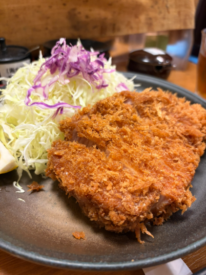 黒い皿に盛られた厚切りのロースカツ。断面はほんのりとピンク色で、肉汁が滲んでいる。横には千切りキャベツが添えられている。